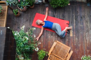A top view of senior woman outdoors on a terrace in summer, doing exercise on mat.