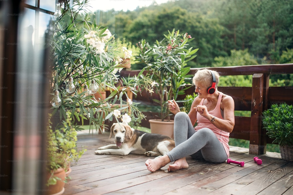 A senior woman with dog and headphones outdoors on a terrace, resting after exercise.