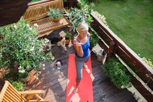 A top view of senior woman outdoors on a terrace in summer, doing exercise with dumbbells.