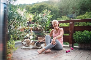 A senior woman with dog and headphones outdoors on a terrace, resting after exercise.