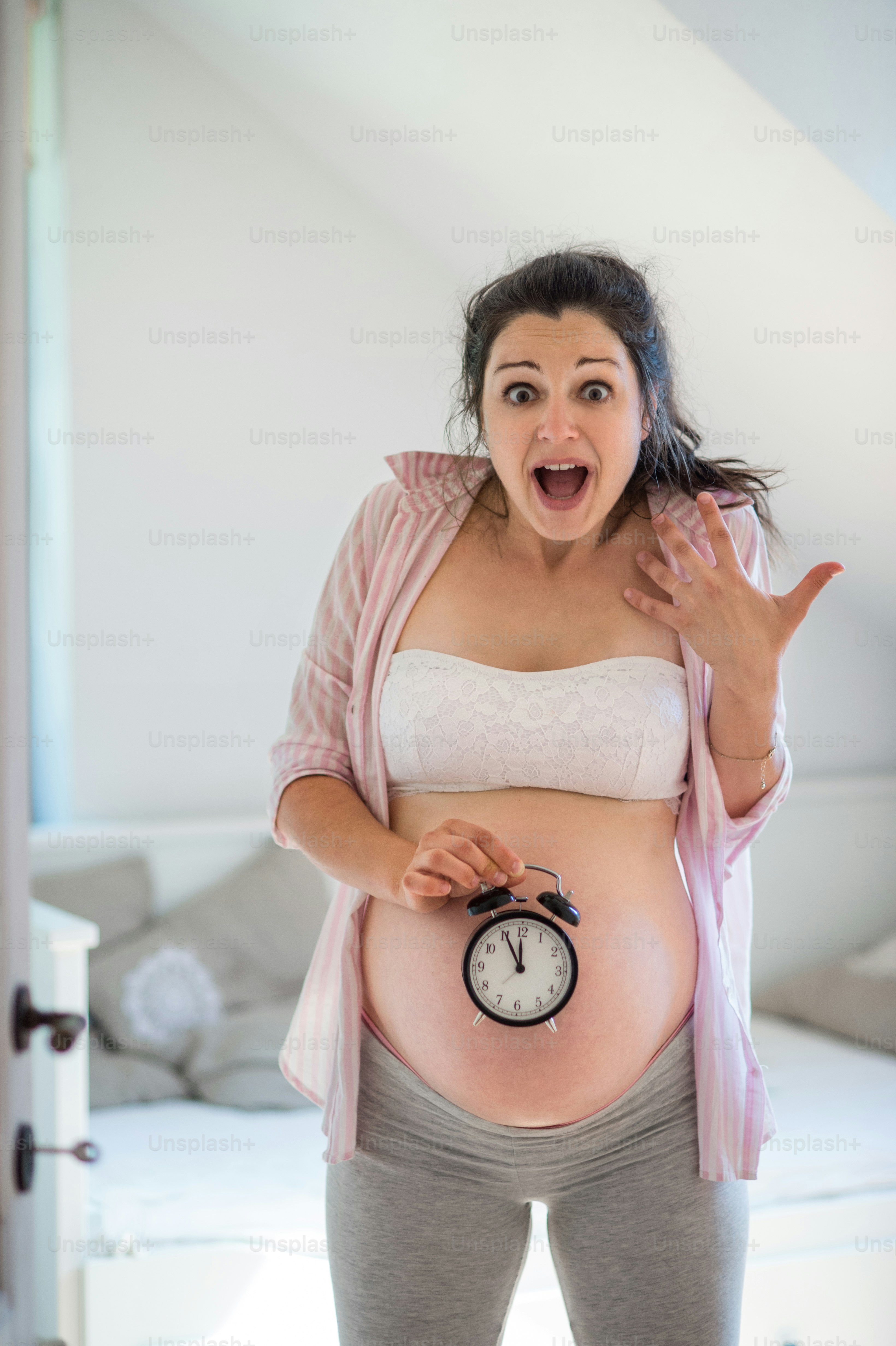 自宅の屋内に時計を持つ幸せな妊婦のポートレート、期日のコンセプト。