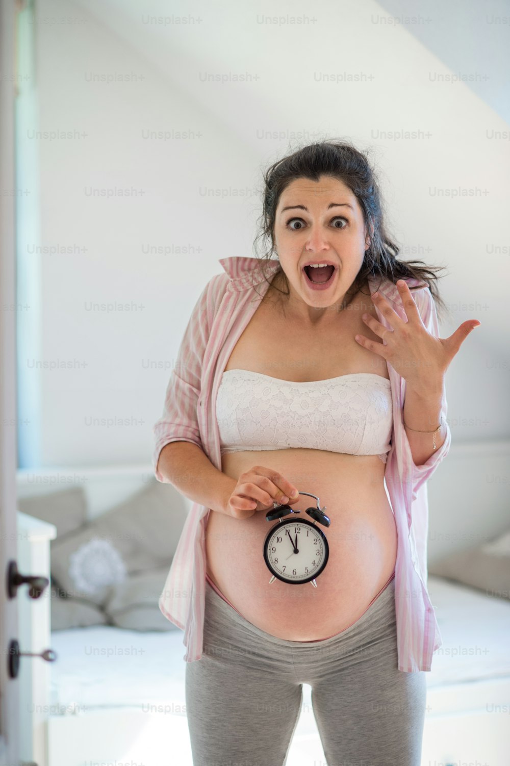 Retrato de mujer embarazada feliz con reloj interior en casa, concepto de fecha de vencimiento.