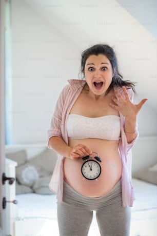 Porträt einer glücklichen schwangeren Frau mit Uhr drinnen zu Hause, Fälligkeitsdatum.
