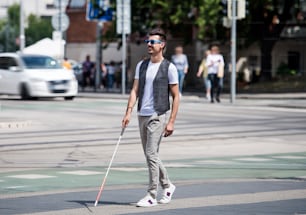白い杖をついた若い盲目の男性が街の通りを横切って歩く。スペースをコピーします。