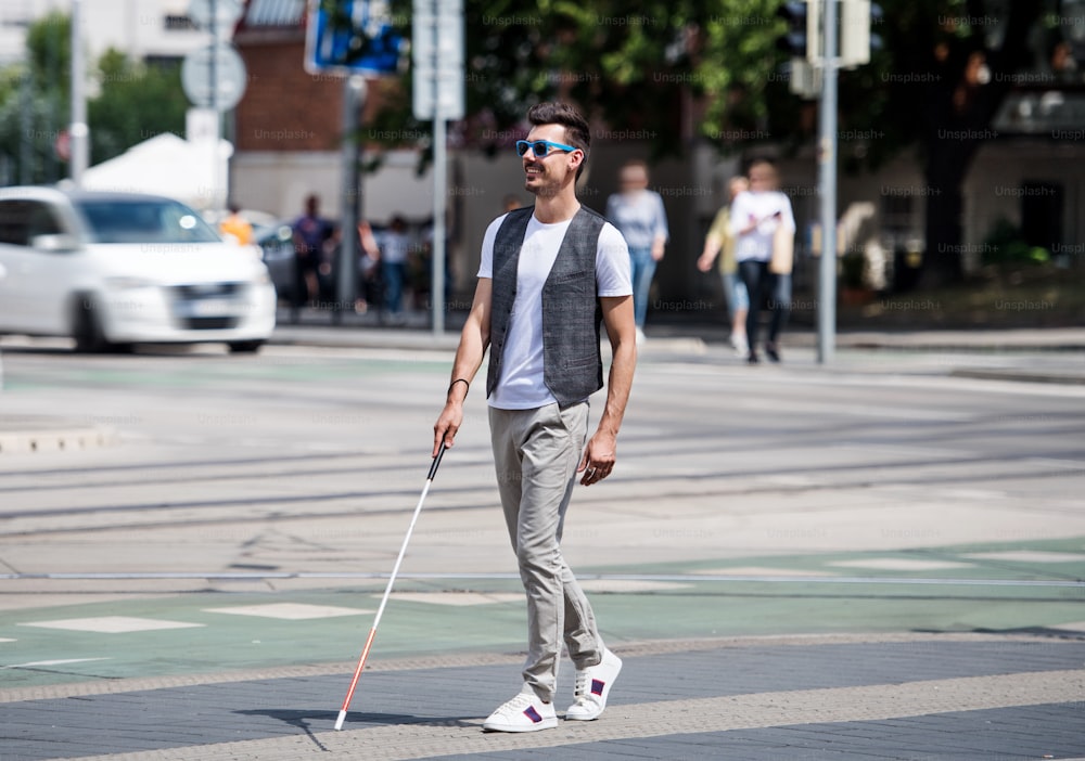 Joven ciego con bastón blanco caminando por la calle en la ciudad. Espacio de copia.