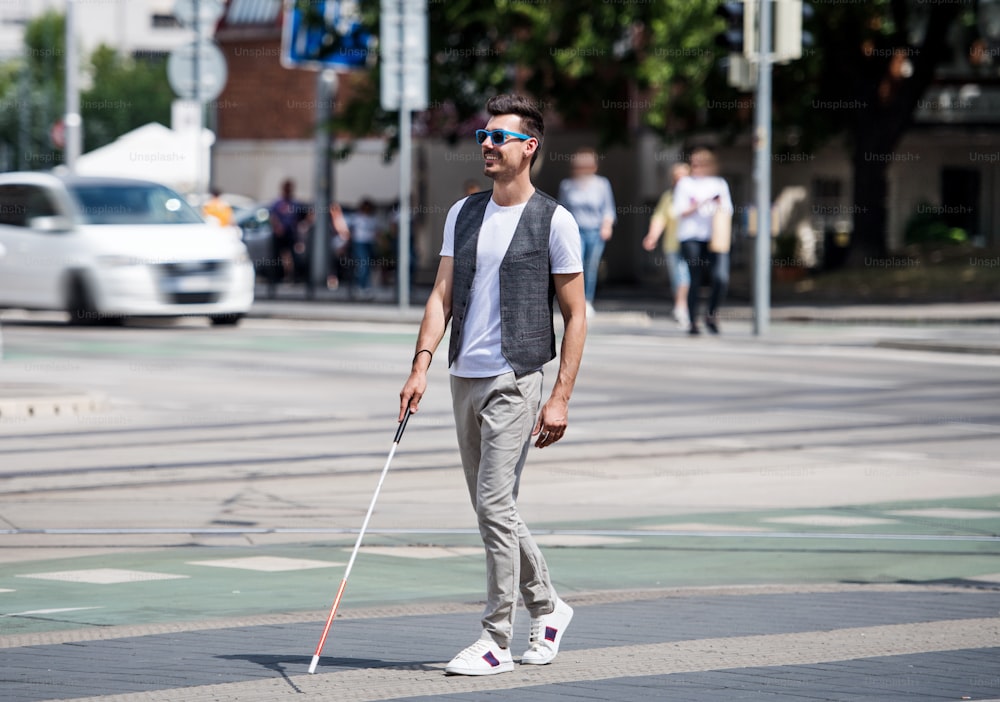 Giovane cieco con bastone bianco che attraversa la strada in città. Copia spazio.