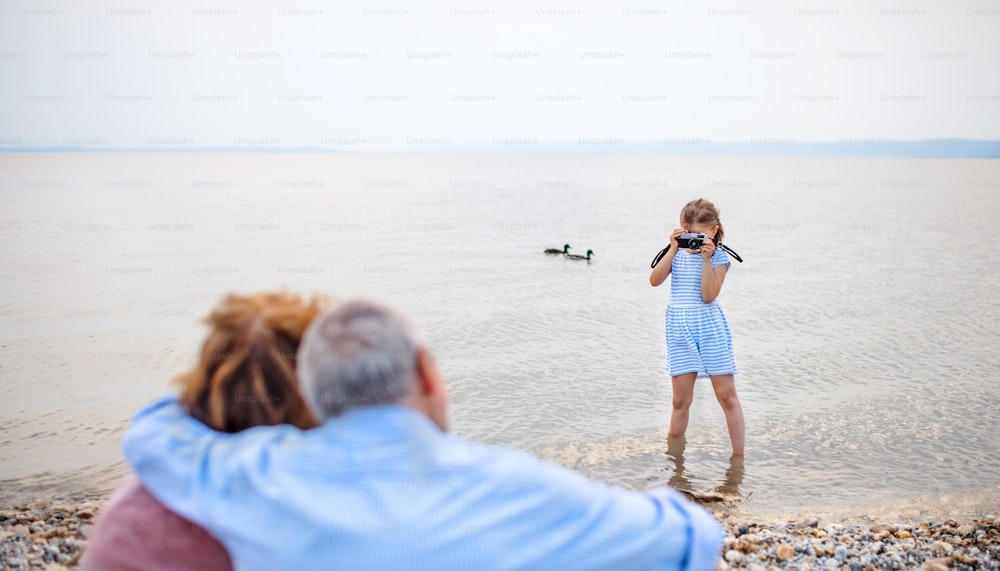 Une petite fille avec appareil photo et grands-parents sur le lac de vacances, prenant des photos.