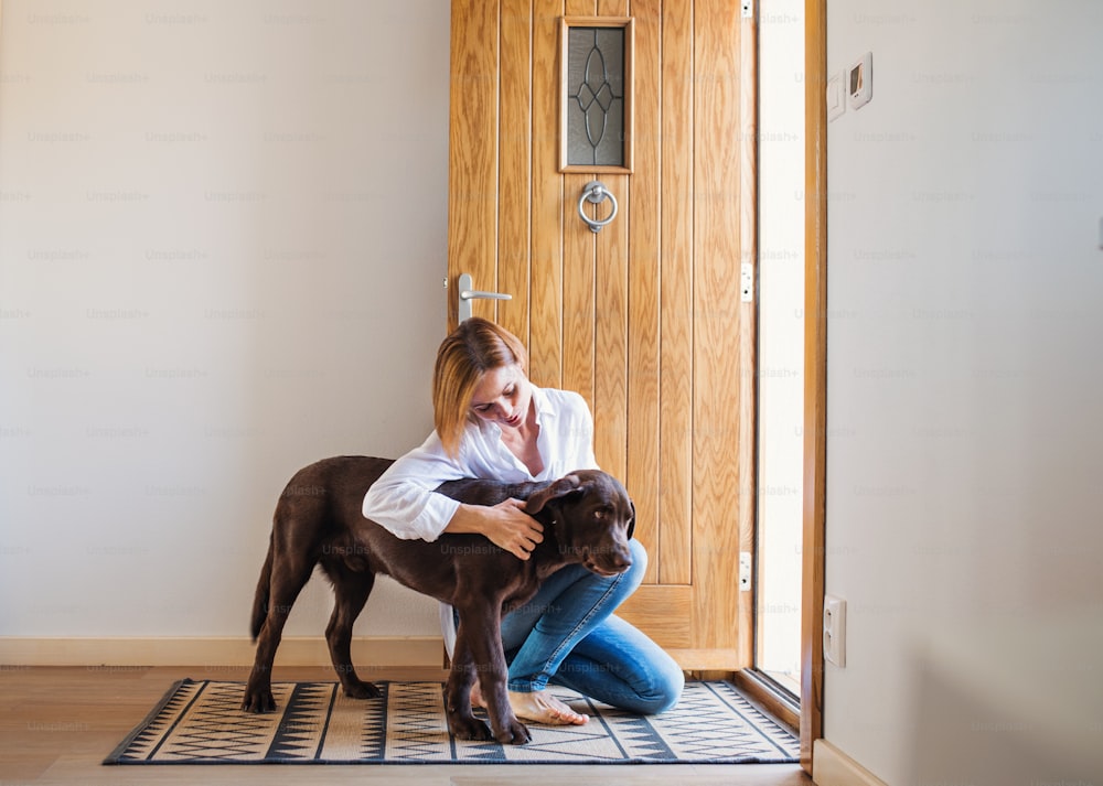 Uma jovem mulher sentada dentro de casa ao lado da porta no chão de casa, brincando com um cachorro. Espaço de cópia.