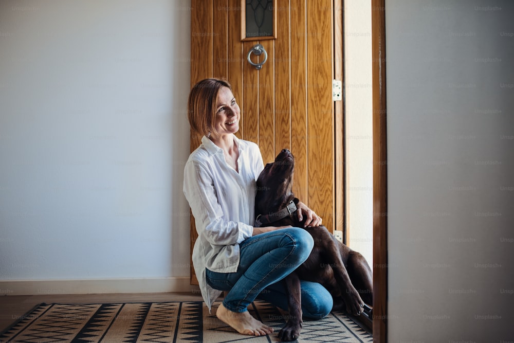 A young woman sitting indoors on the floor at home, playing with a dog at the door.