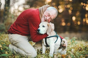 Ein glücklicher älterer Mann mit einem Hund auf einem Spaziergang in einer herbstlichen Natur bei Sonnenuntergang.