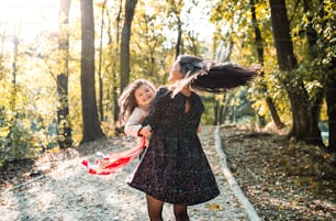 Eine Rückansicht einer jungen Mutter mit einer kleinen Tochter im Wald in der Herbstnatur, die Spaß hat.