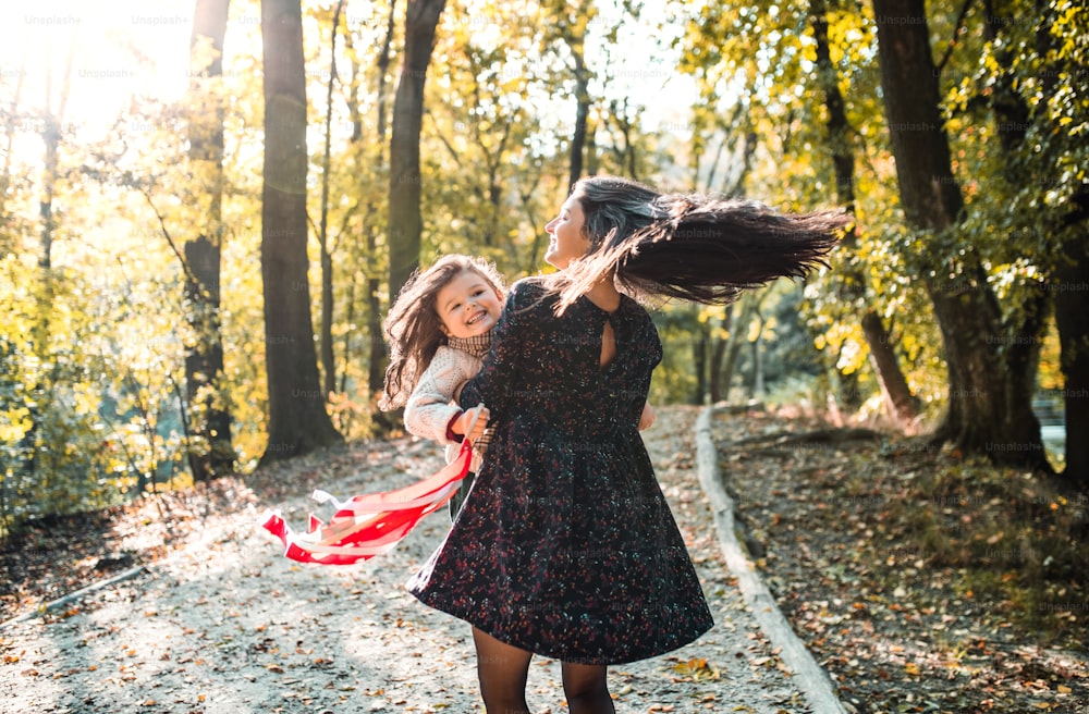 Uma visão traseira da jovem mãe com uma filha pequena na floresta na natureza do outono, se divertindo.