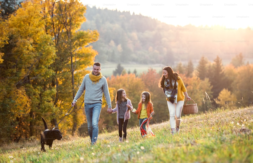 Uma jovem família com duas crianças pequenas e um cão preto em um passeio na natureza do outono.