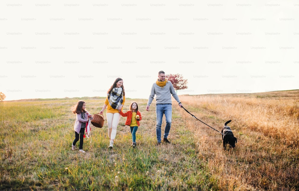 Una giovane famiglia con due bambini piccoli e un cane nero in una passeggiata nella natura autunnale.