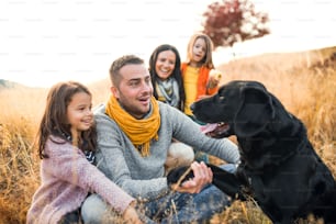 A young family with two small children and a black dog on a meadow in autumn nature.
