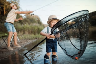 Un père d’âge mûr avec un petit fils en bas âge qui pêche à l’extérieur au bord d’une rivière ou d’un lac.