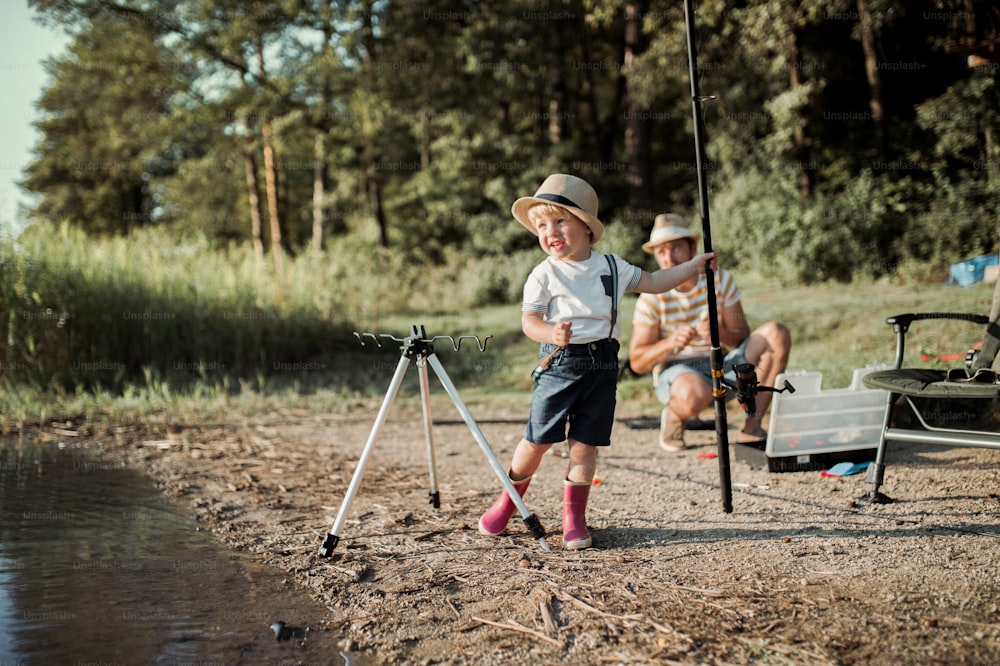 Un padre maturo con un piccolo figlio piccolo che pesca all'aperto vicino a un fiume o un lago.