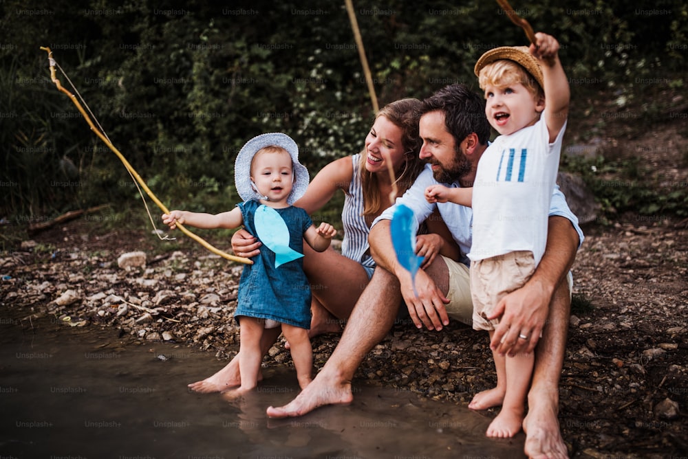 Una familia joven con dos niños pequeños que pasan tiempo al aire libre junto al río en verano.