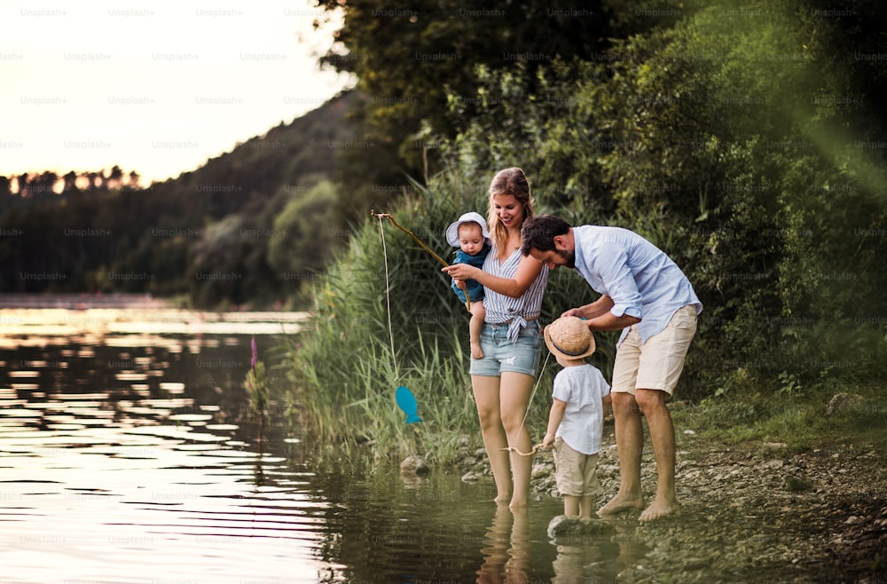 Uma jovem família com duas crianças pequenas que passam o tempo ao ar livre à beira do rio no verão.