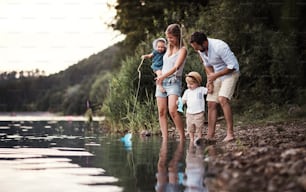 A young family with two toddler children spending time outdoors by the river in summer.