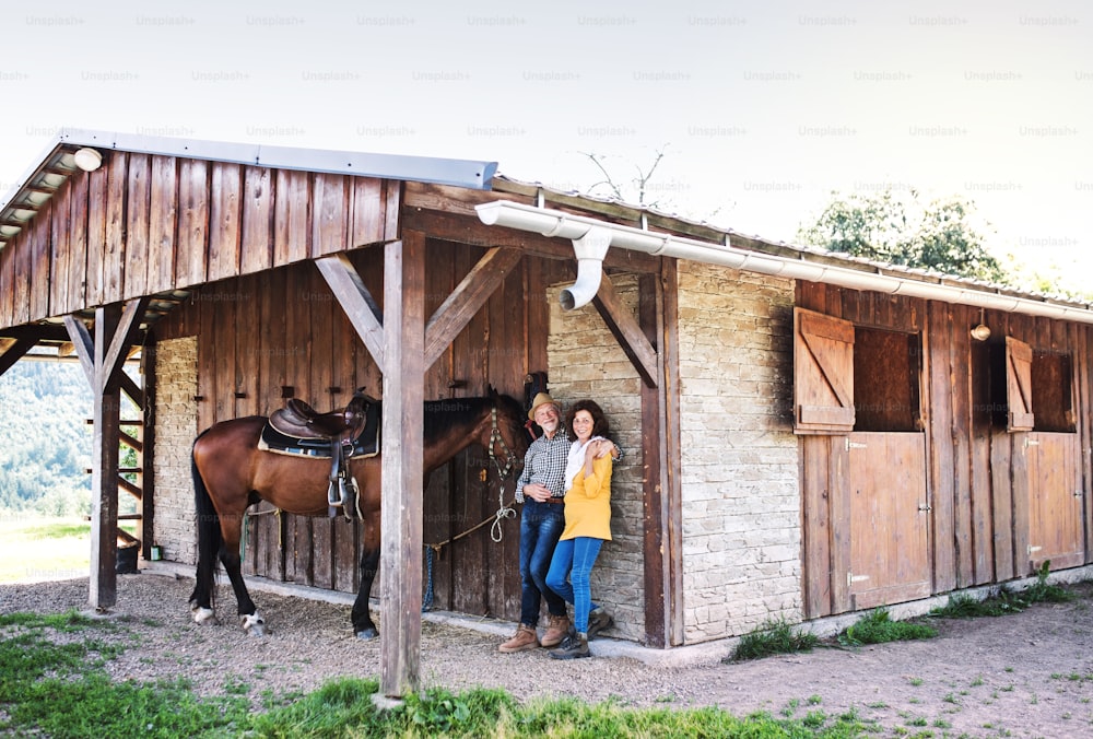 Una coppia anziana con un cavallo marrone in piedi di fronte a una stalla di legno.