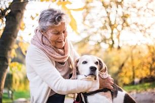 An elderly woman with dog in autumn nature. Senior woman on a walk.