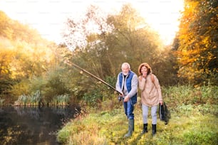Pareja de ancianos activa pescando en el lago. Una mujer y un hombre en una hermosa naturaleza otoñal temprano en la mañana.