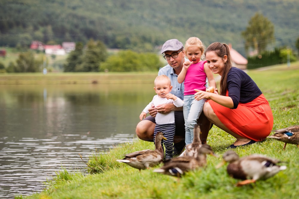 Happy young family spending time together outside in green nature, sitting in a grass on a lake bank.
