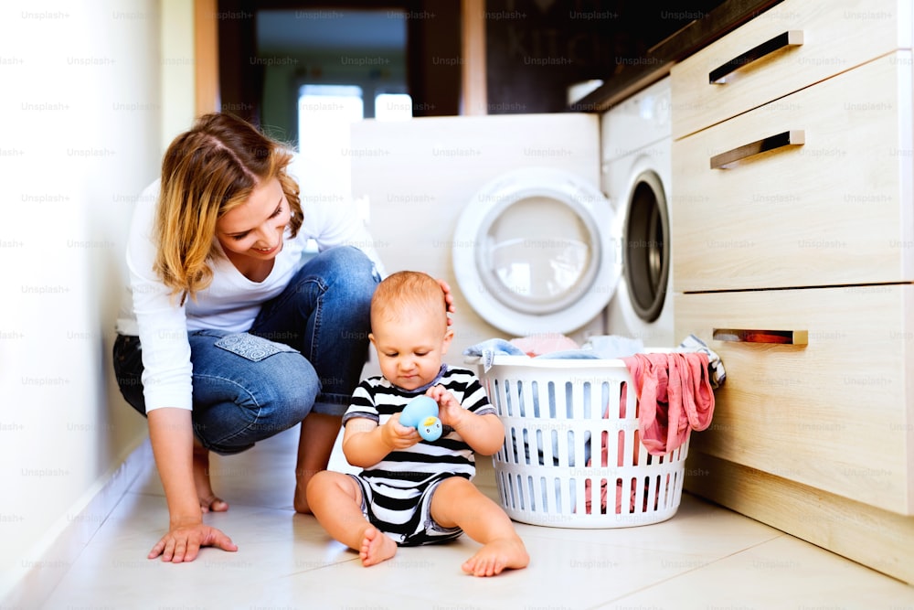 Madre joven con un bebé haciendo las tareas domésticas. Hermosa mujer y bebé lavando la ropa.