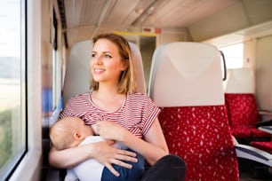 Young mother travelling with baby boy by train. Railway journey of a beautiful woman and her son.