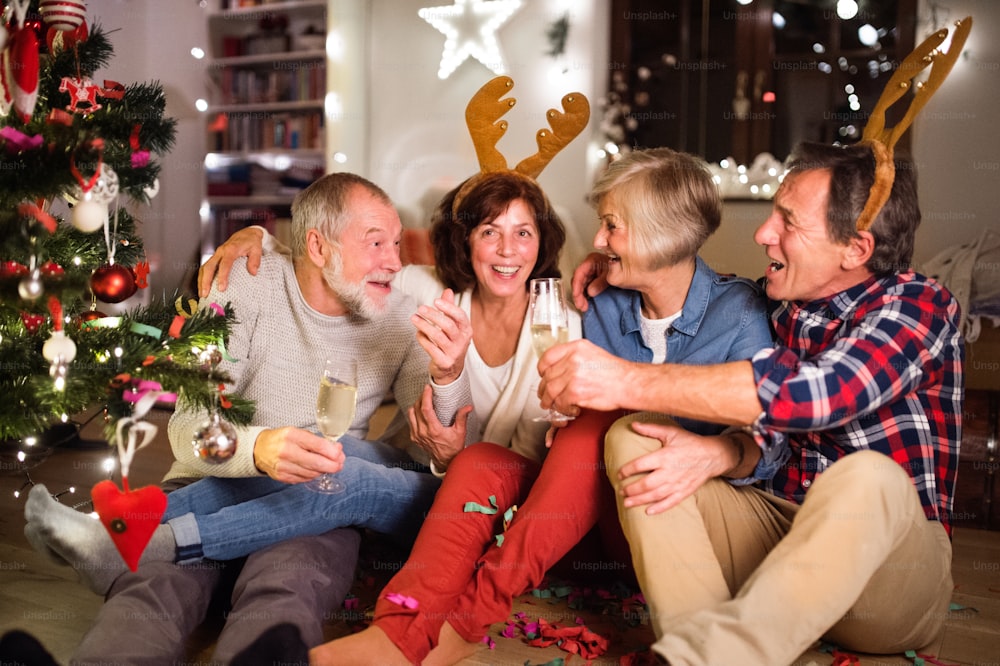 Ältere Freunde, die zur Weihnachtszeit Stirnbänder mit Rentiergeweihen tragen, Wein trinken und Spaß haben.