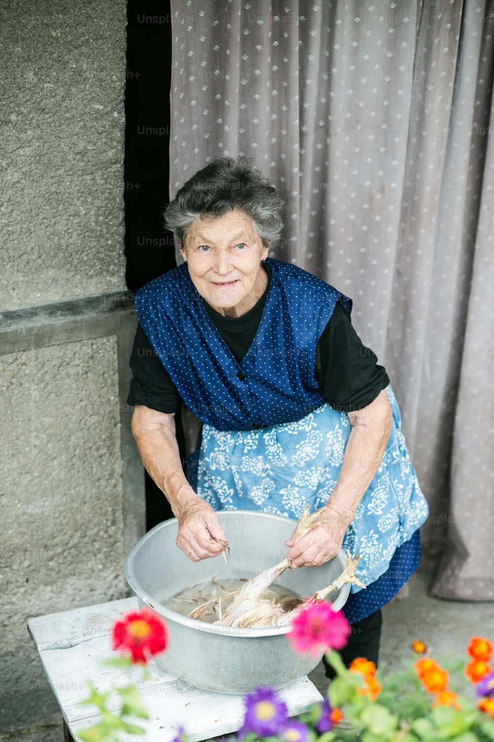 Mulher idosa limpando e lavando frango recém-abatido do lado de fora na frente de sua casa.