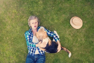 Hermosa mujer mayor con un perro acostado en una hierba
