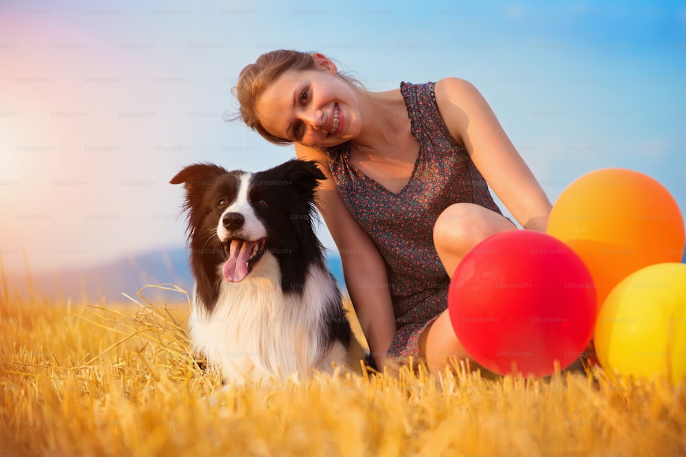 Attraktive junge Frau draußen auf einem Feld mit einem Hund und Ballons.