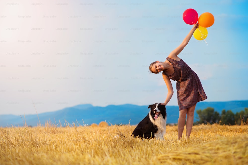 Attraktive junge Frau draußen auf einem Feld mit einem Hund und Ballons.