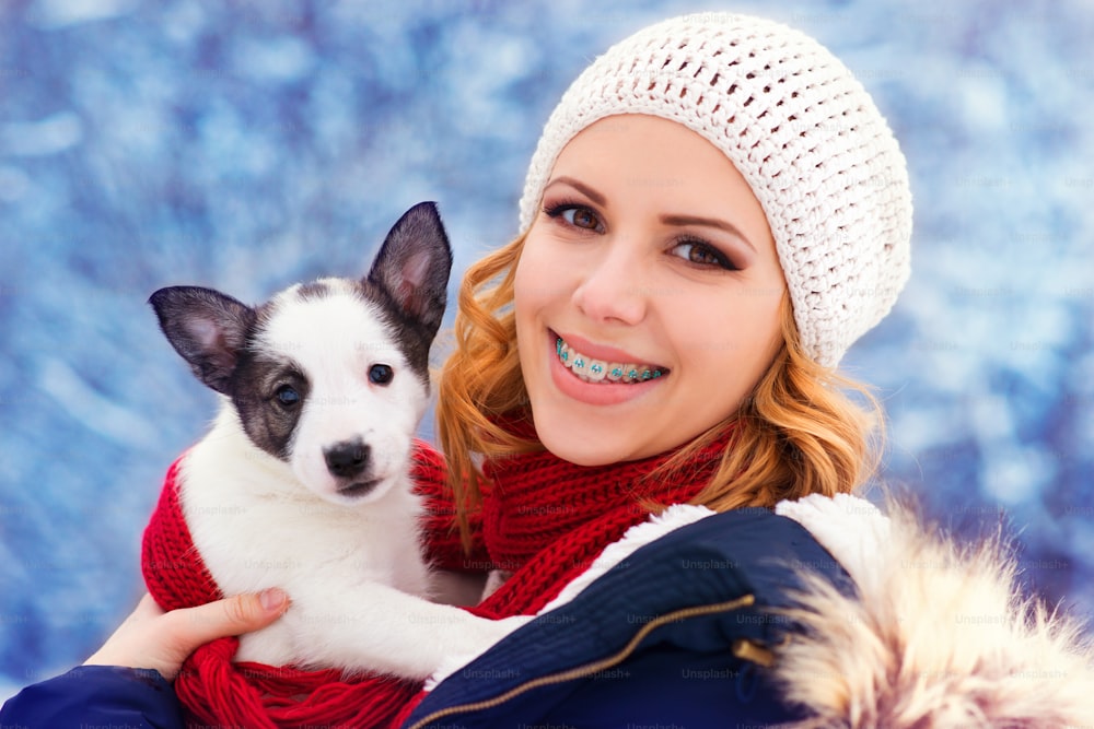 Mulher jovem atraente que se diverte fora na neve com seu filhote de cachorro do cão