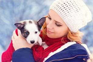 Attraktive junge Frau, die mit ihrem Hundewelpen draußen im Schnee Spaß hat