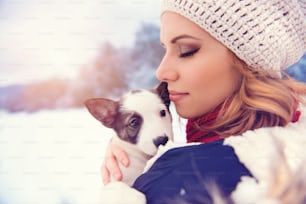Attraktive junge Frau, die mit ihrem Hundewelpen draußen im Schnee Spaß hat