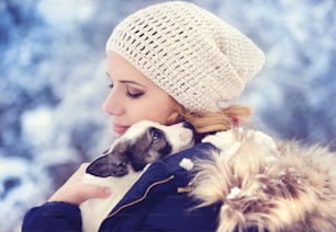 Mulher jovem atraente que se diverte fora na neve com seu filhote de cachorro do cão