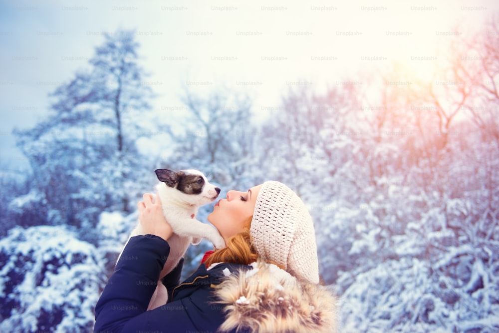 Giovane donna attraente che si diverte fuori nella neve con il suo cucciolo di cane