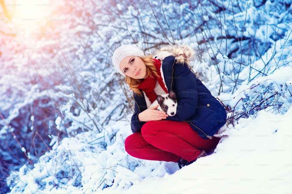 Giovane donna attraente che si diverte fuori nella neve con il suo cucciolo di cane