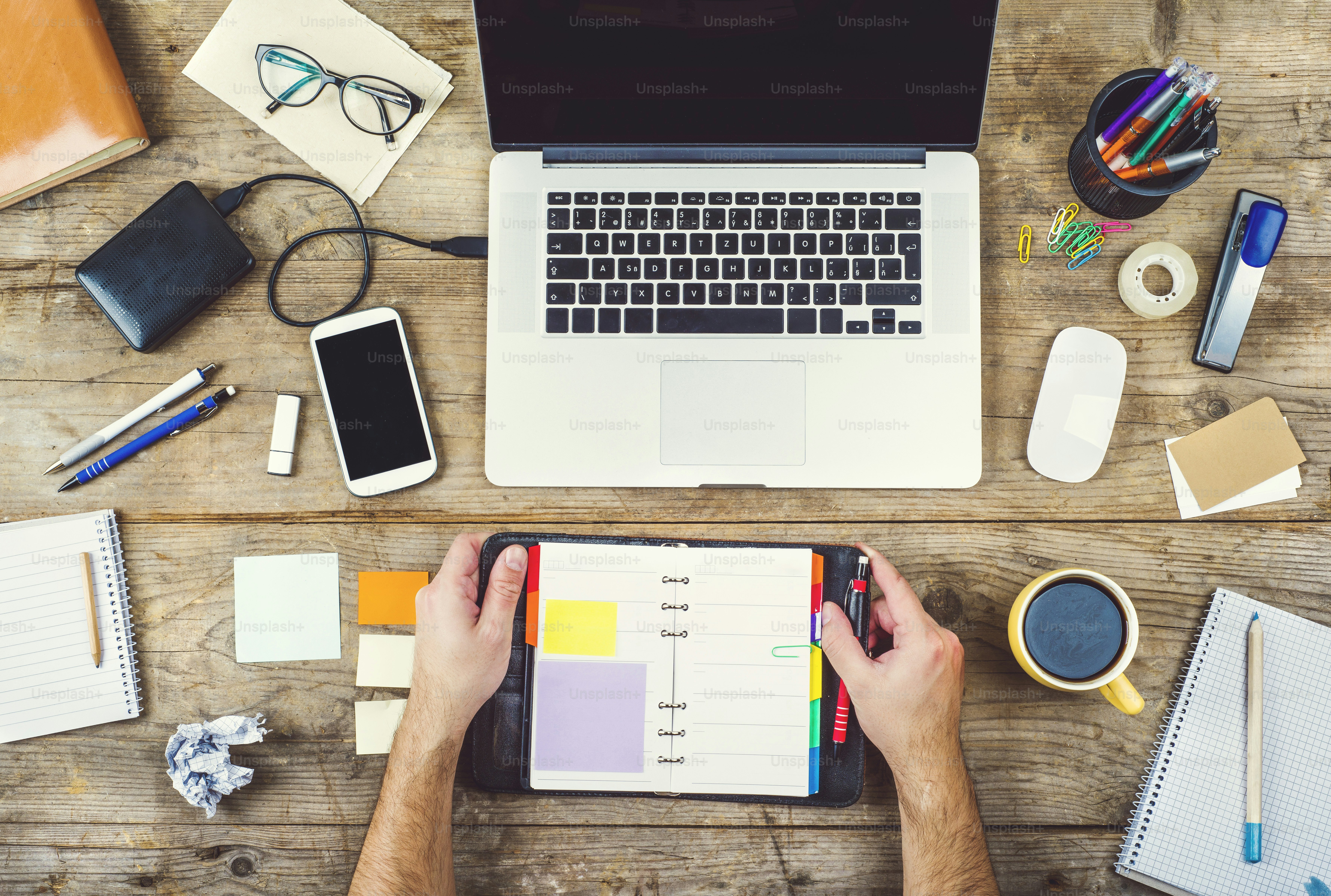 Mix of office supplies and gadgets on a wooden desk background. View from above.