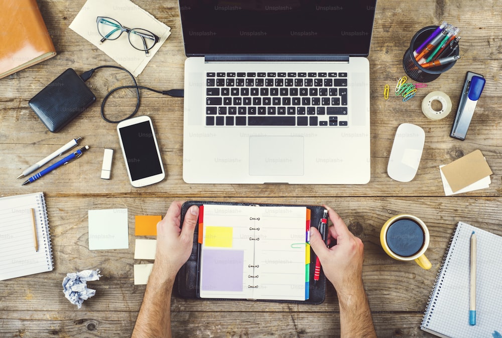 Mix of office supplies and gadgets on a wooden desk background. View from above.