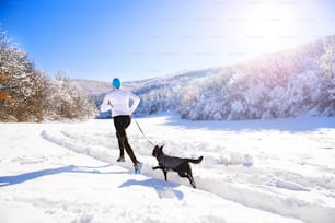 Young sportsman jogging with dog outside in sunny winter park