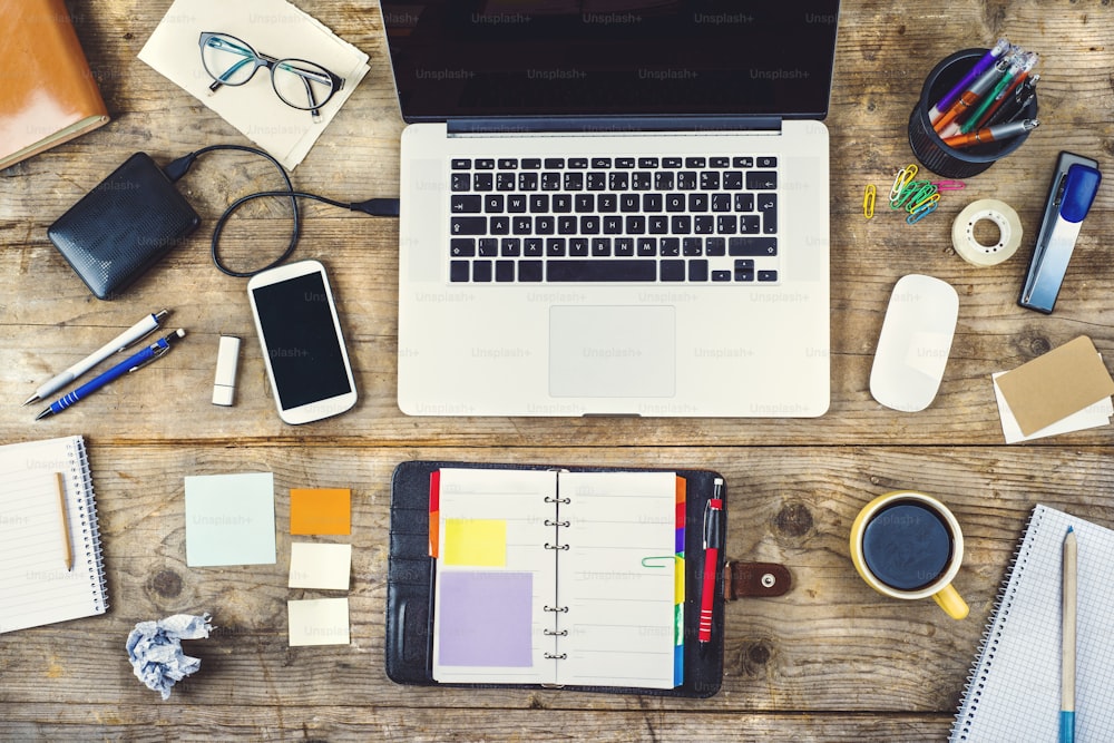 Mix of office supplies and gadgets on a wooden desk background. View from above.