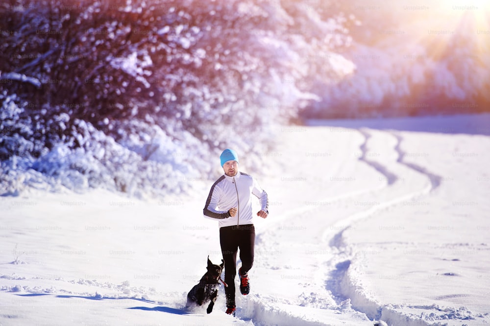 Junger Sportler joggt mit Hund draußen im sonnigen Winterpark