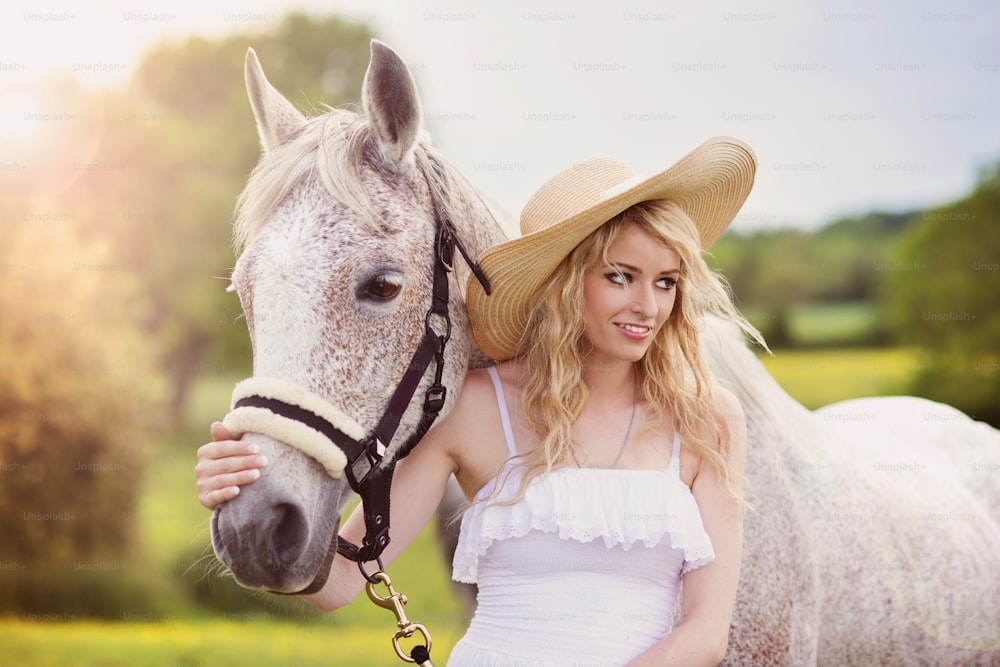 緑の田園地帯で馬と歩く白いドレスを着た女性