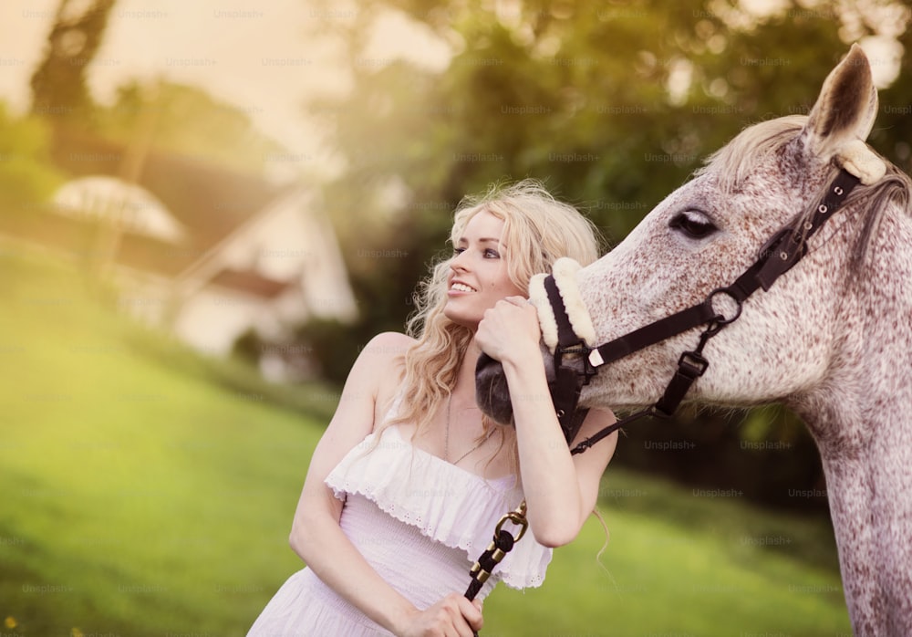 Donna in vestito bianco che cammina con il cavallo nella campagna verde