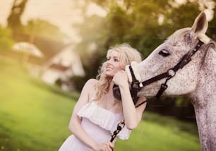 Woman in white dress walking with horse in green countryside