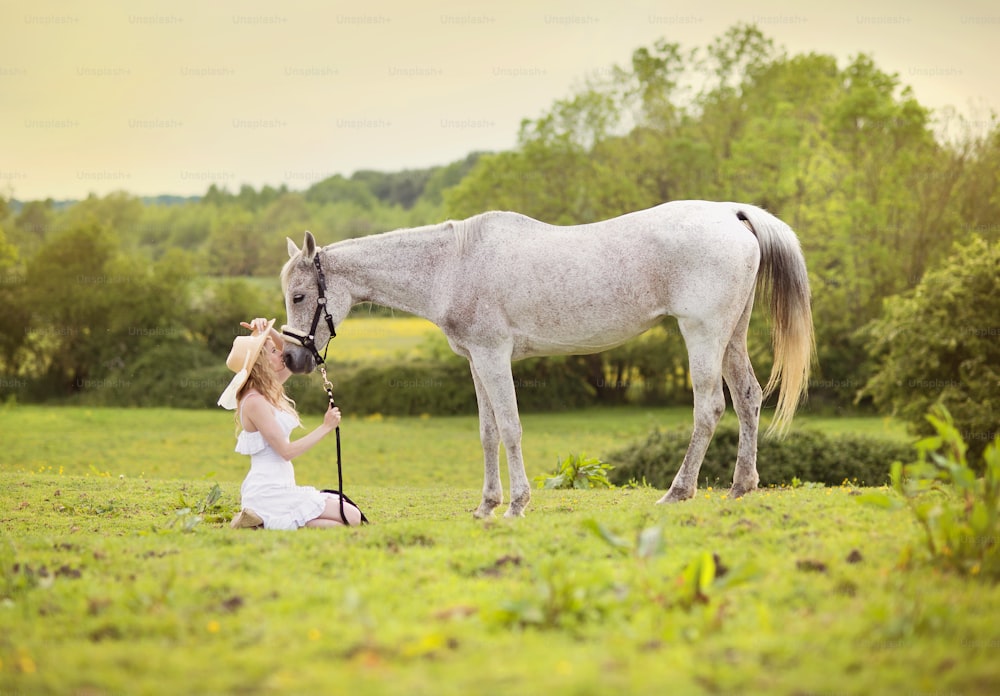 하얀 드레스를 입은 여자가 녹색 시골에서 말과 함께 걷고 있다